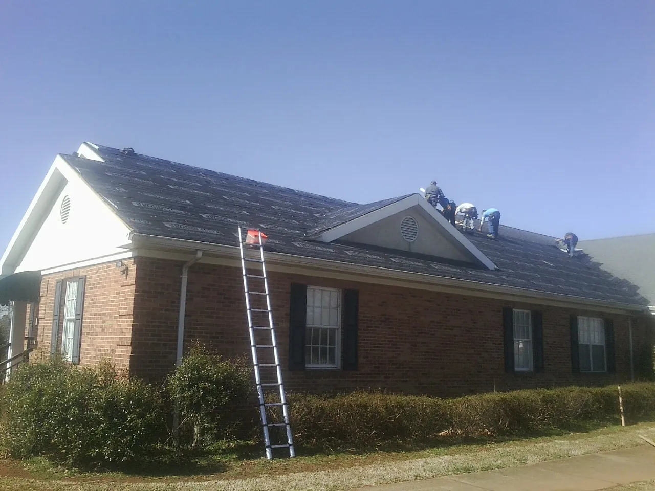 Crew tearing shingles off a brick ranch roof with a ladder set — Emergency Roof Repair work by our crew in Canistota