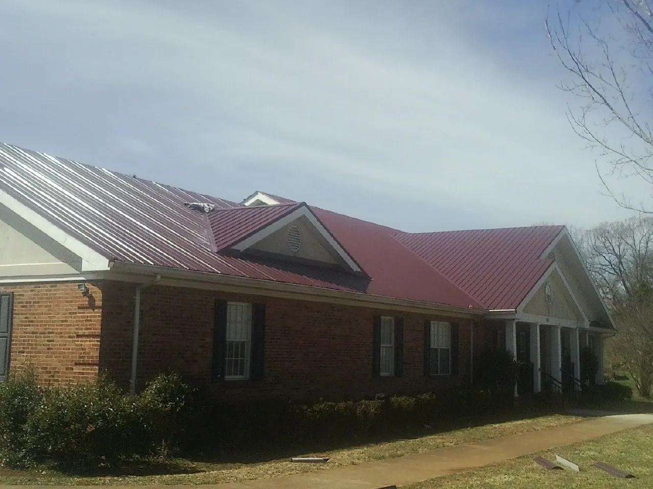 Red metal roof with gabled entries on a long brick building, from a Hail Damage Roof Repair job in Canistota