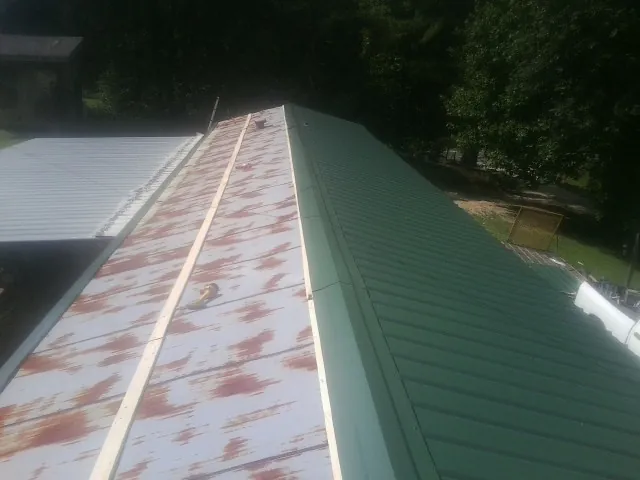 Old rusted panels beside newly installed green metal roofing — Wind Damage Roof Repair by Roofing Brothers in Canistota