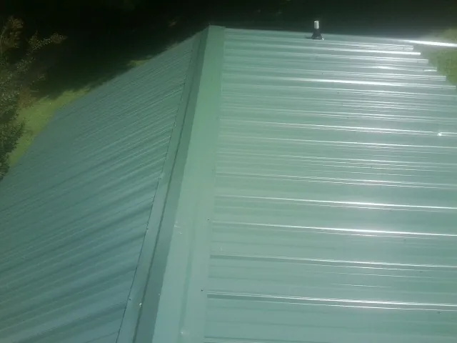 New green metal panels meeting at the ridge of a roof — Flat Roof Repair work by our crew in Canistota