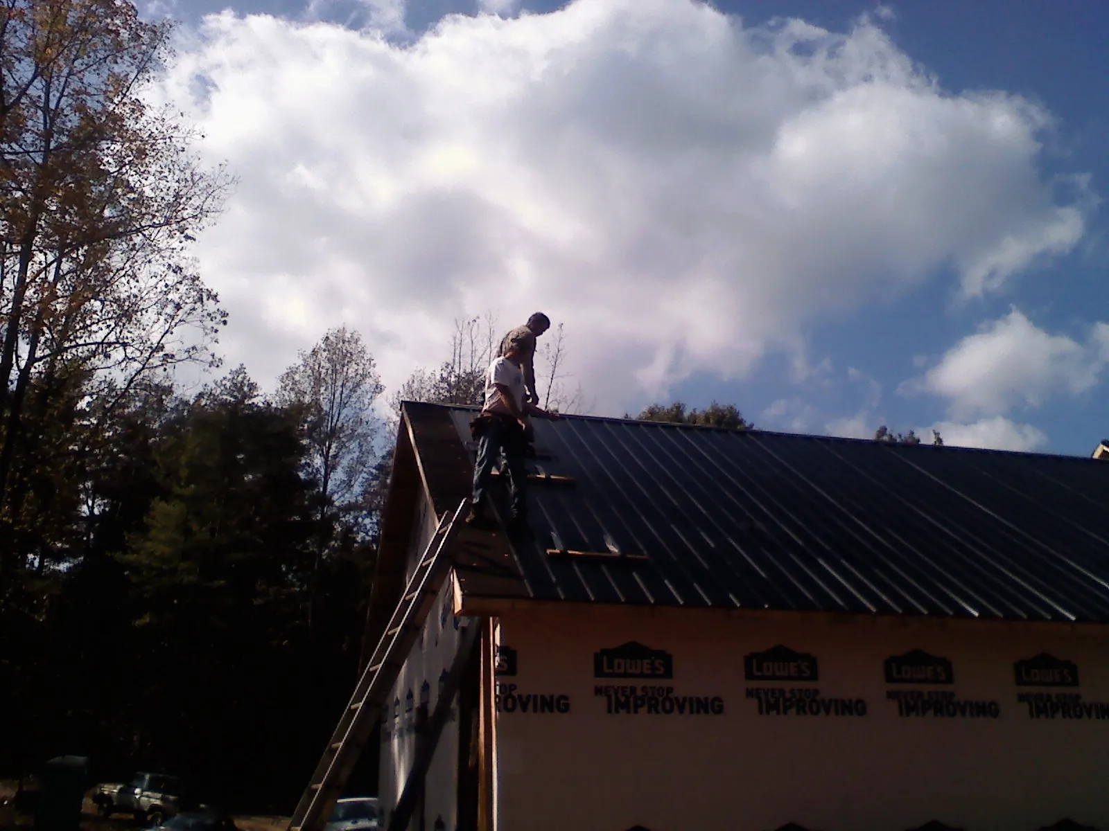 Roofer fastening dark metal panels high against a cloudy sky, from a Roof Inspection job in Canistota