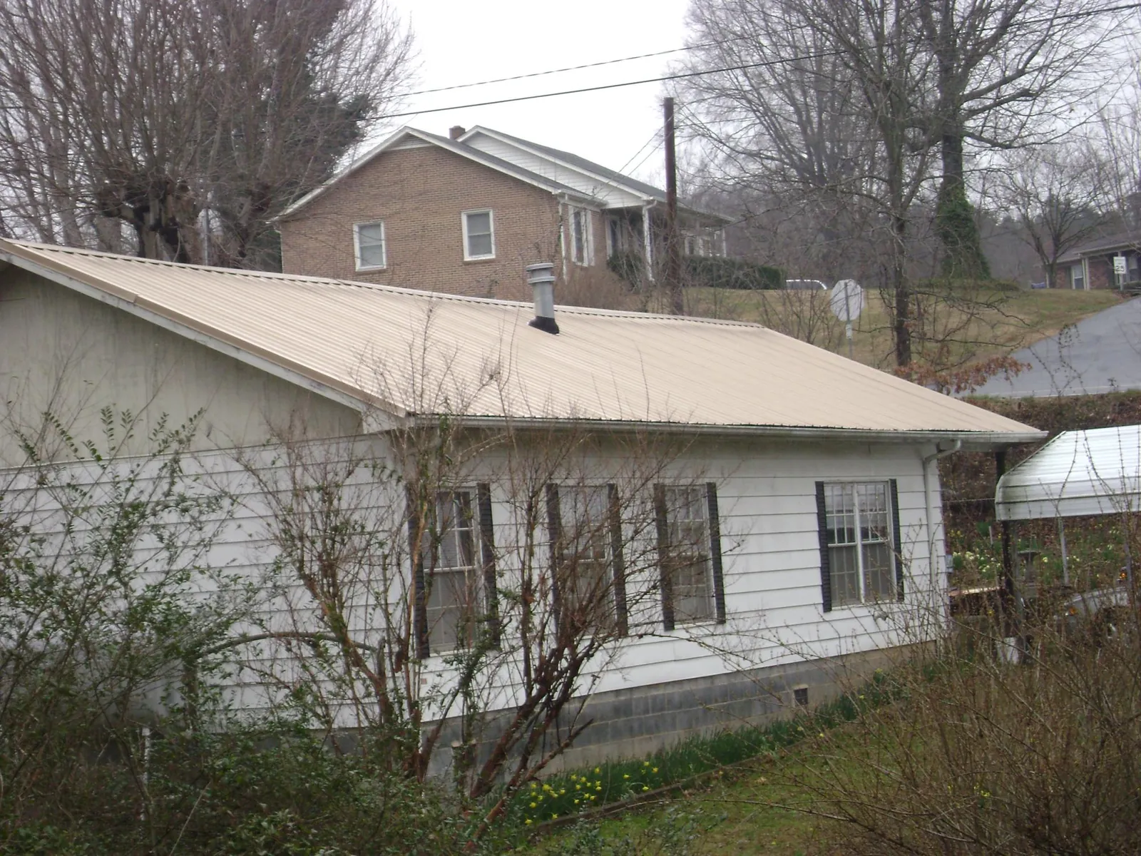 Tan metal roof on a white sided house set into a hillside — Commercial Roofing by Roofing Brothers in Canistota